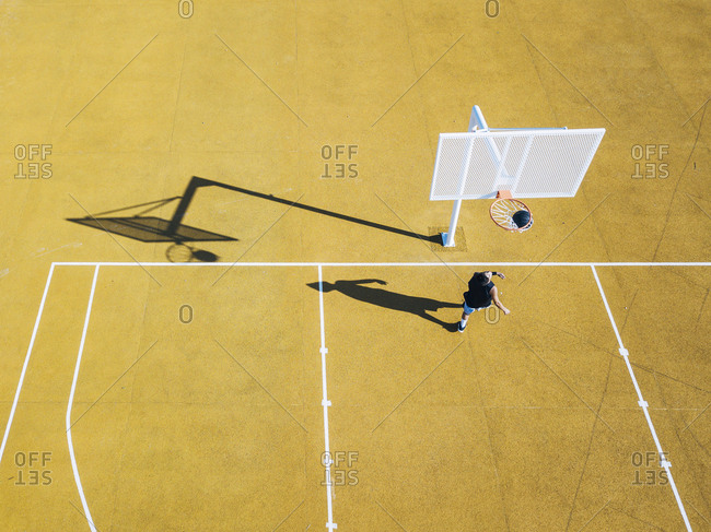 Young man playing basketball on outdoor court. Top view, bird eye view of yellow basketball court