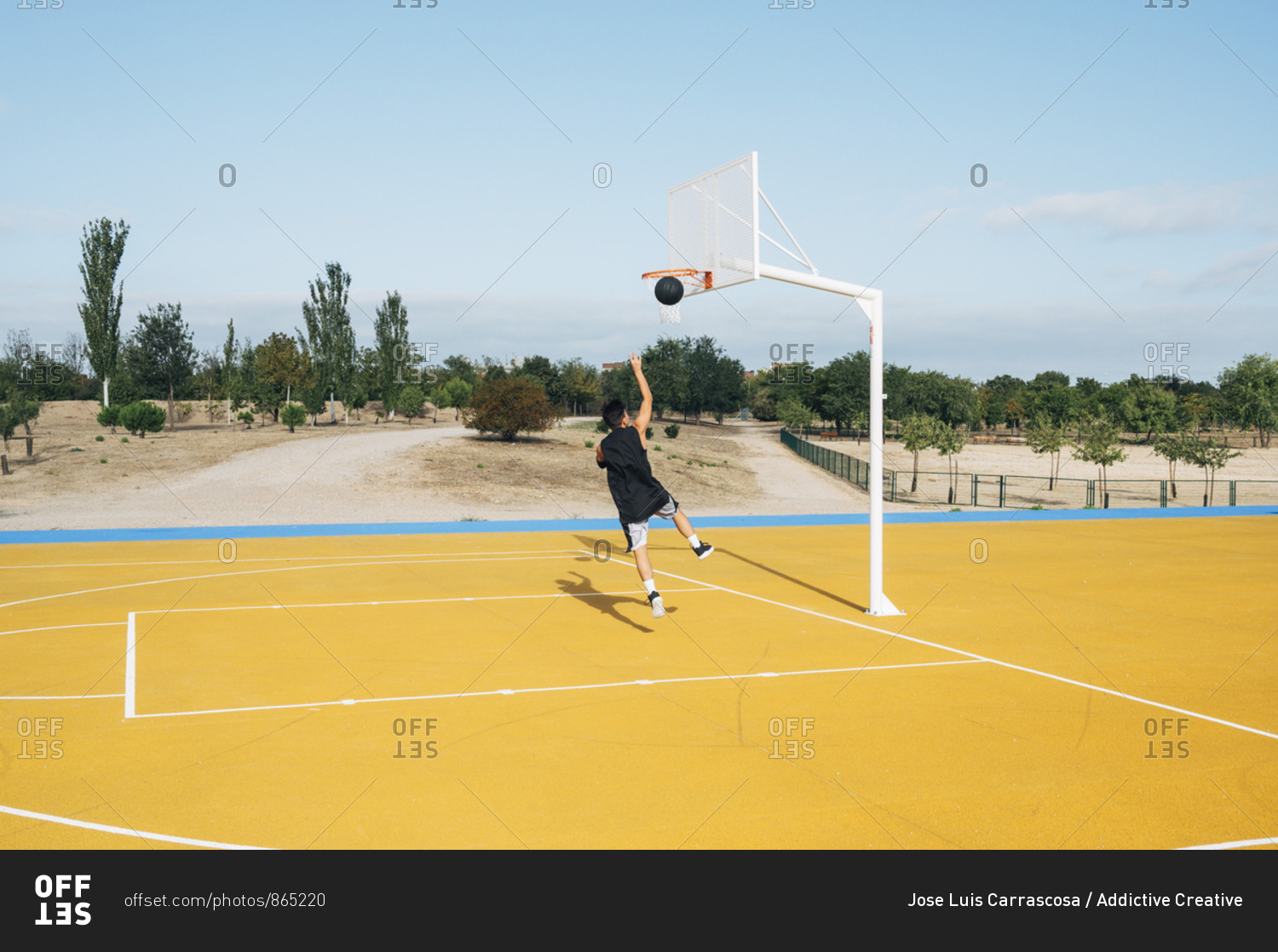 Young man playing on yellow basketball court outdoor.
