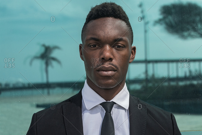 African American young confident severe pensive businessman in corporate suit looking at camera on glass background with reflection