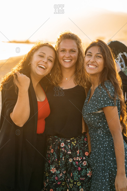 A colorful portrait of three beautiful women hugging on the beach with the sun behind them Vacation concept Vertical image