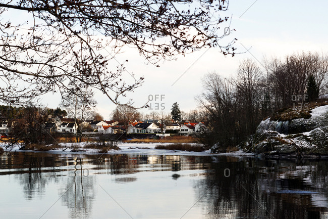 Winter river bank with leafless trees and colorful houses in distance