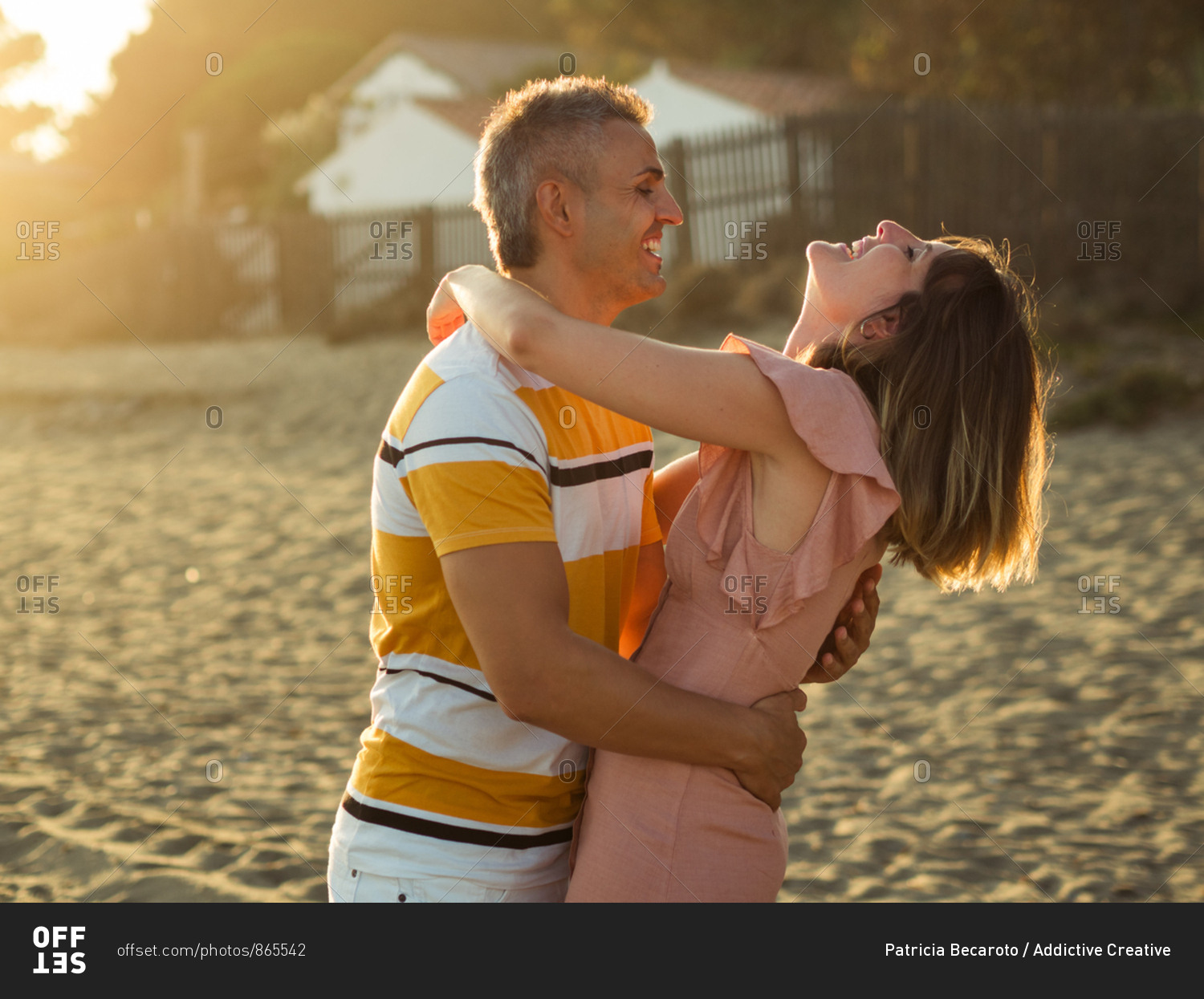 Excited adult man and woman laughing and embracing each other while having fun on sandy shore on resort