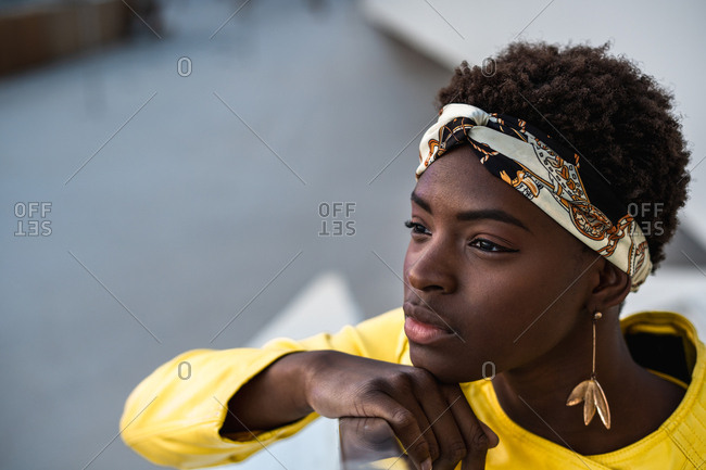 High angle of glad African American woman in stylish wear chilling on stairs leaning on the handrail and looking away
