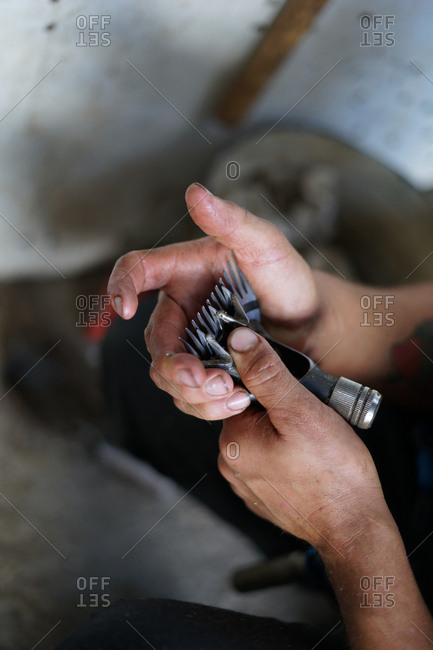 anonymous man fixing dirty shearing razor while working in barn on farm