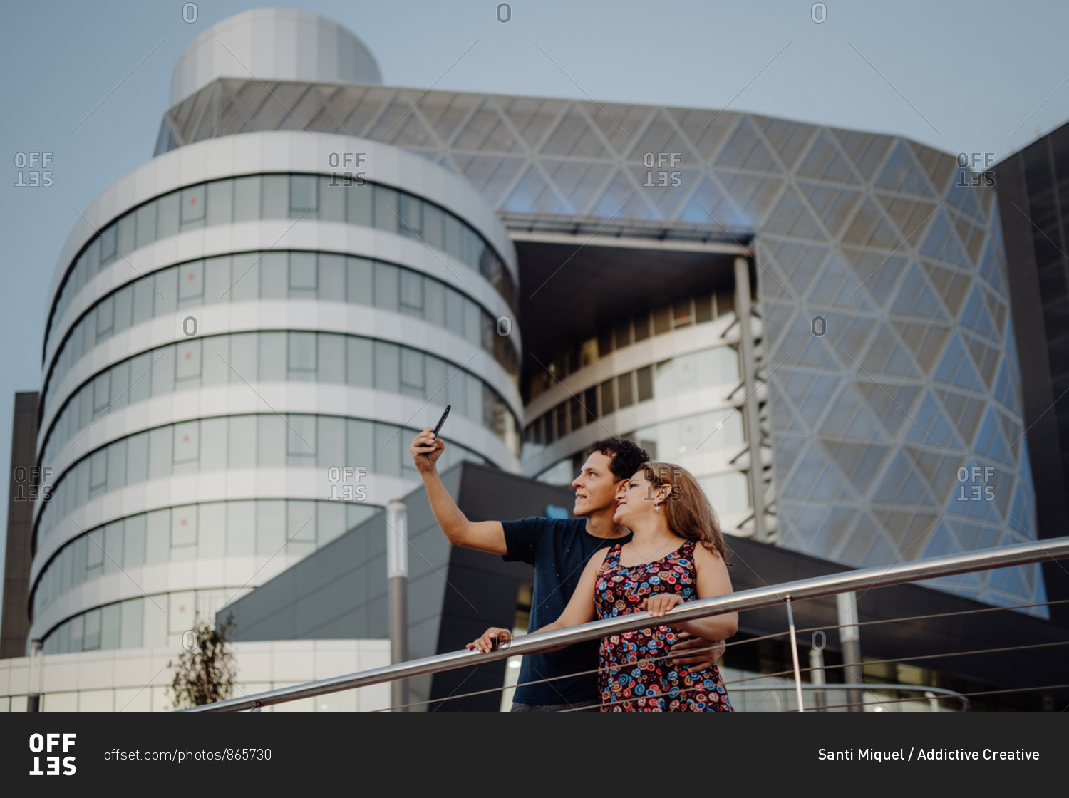 Romantic traveling couple taking selfie on mobile phone on background of amazing geometric building in balcony