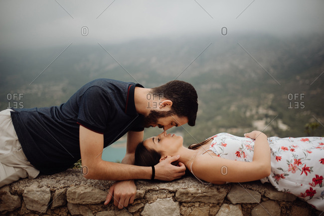 Side view of loving casual man and woman lying on stone parapet of viewpoint at majestic hazy valley
