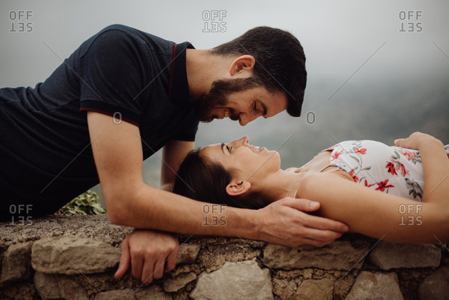 Side view of loving casual man and woman lying on stone parapet of viewpoint at majestic hazy valley
