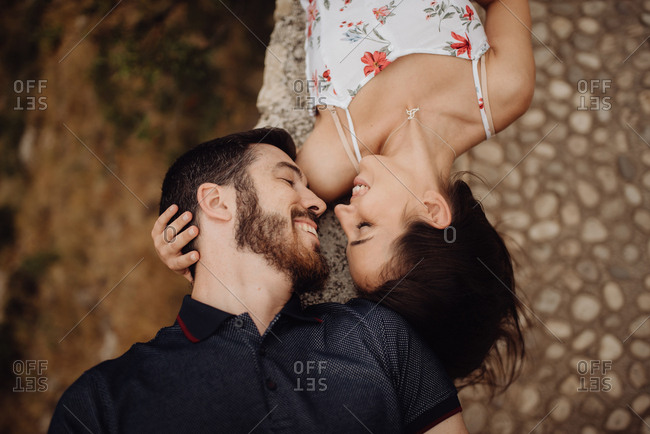 Side view of loving casual man and woman lying on stone parapet of viewpoint at majestic hazy valley