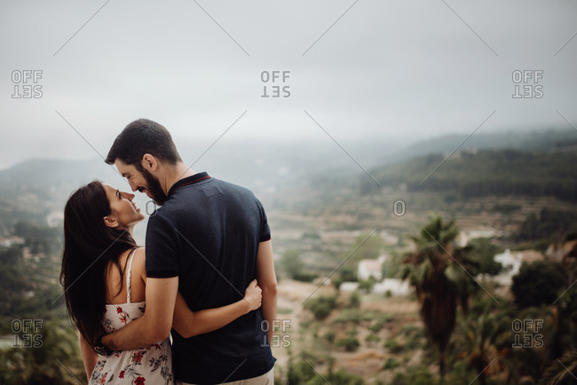 Side view of loving casual man and woman lying on stone parapet of viewpoint at majestic hazy valley