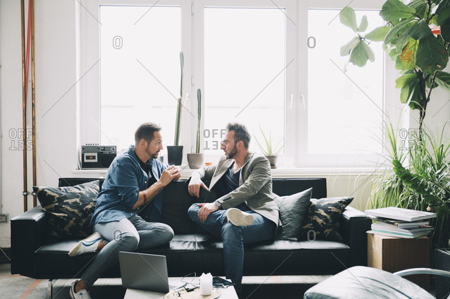 Confident male colleagues discussing while sitting on sofa in creative office