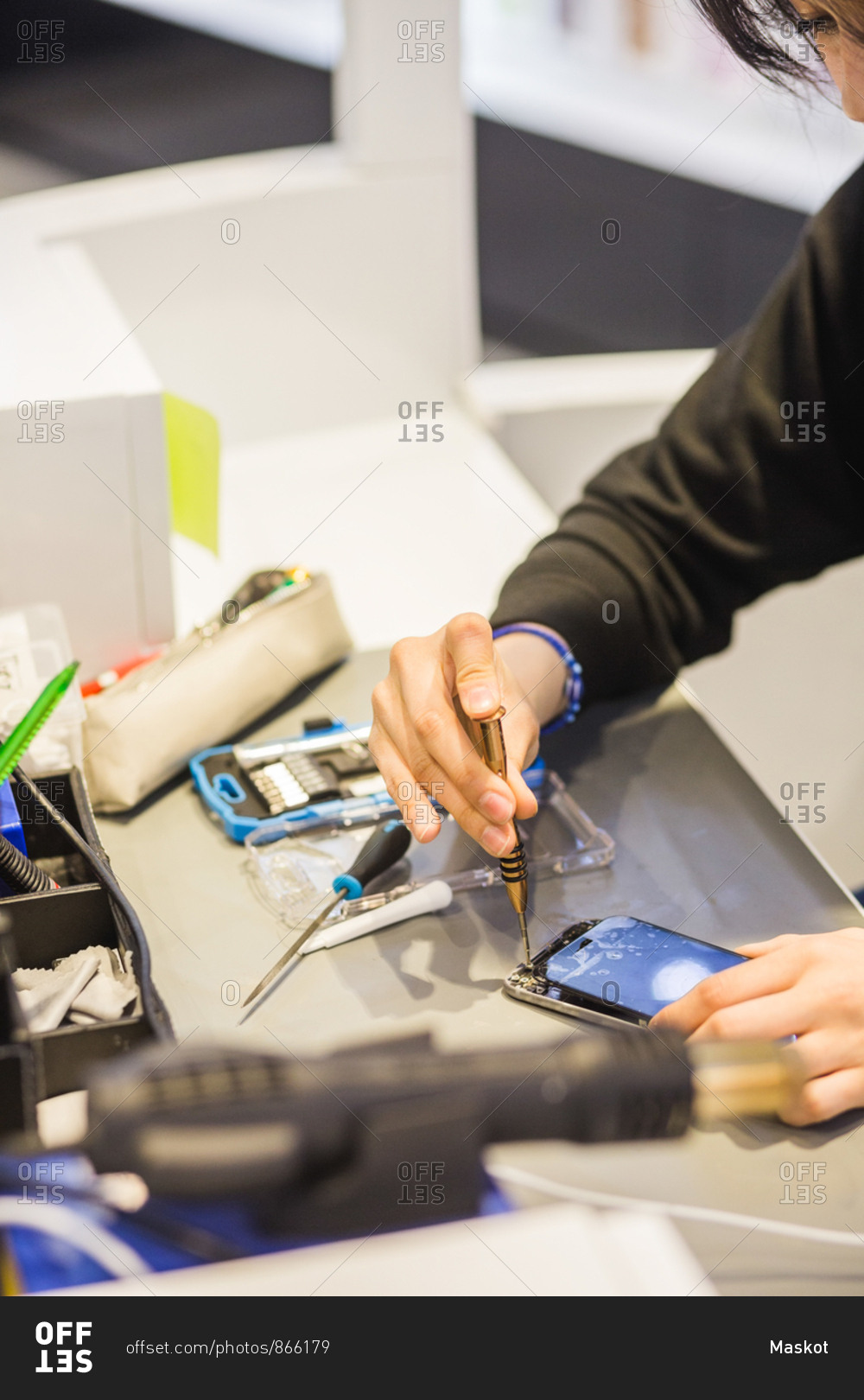 High angle view of young female employee repairing damaged smart phone at illuminated desk in mobile repair shop