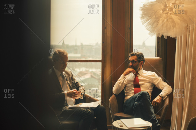 Male financial advisors discussing while sitting against window at law office