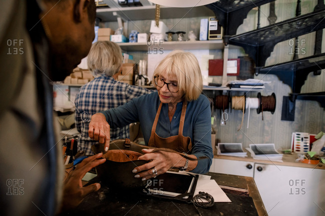 Senior saleswoman explaining leather purse to male customer at checkout in store