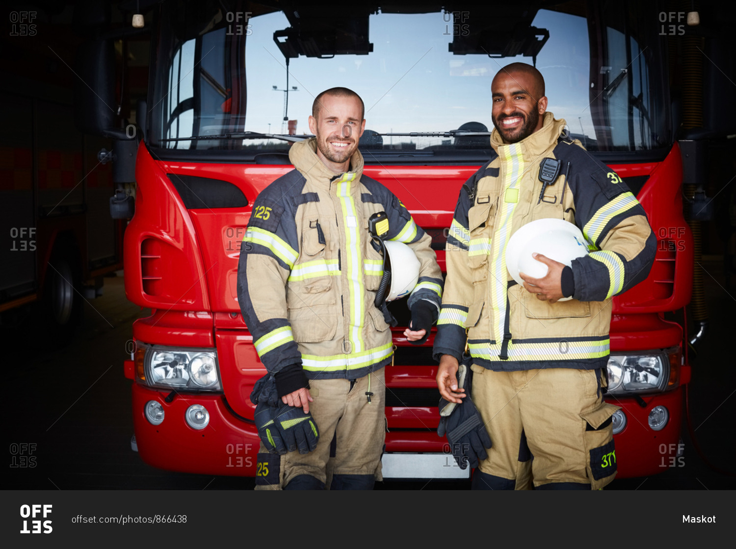 Portrait of coworkers standing in front of fire engine at fire station