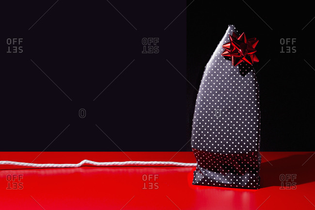 Flat iron wrapped as a gift in polka dot paper with a red bow on black background