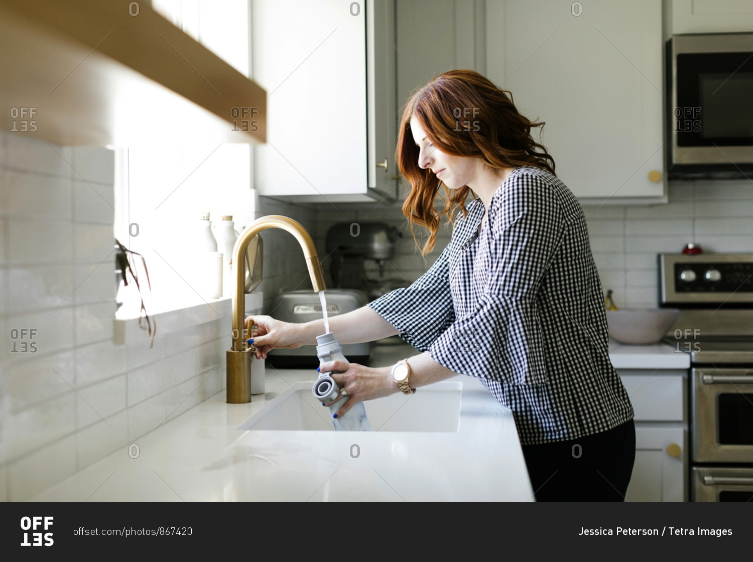Woman filling water bottle in kitchen sink