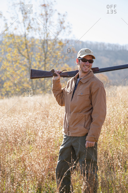 Smiling young man holding rifle in field