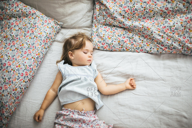 Portrait from above of a toddler girl napping on a bed in a bright room surrounded by pillows