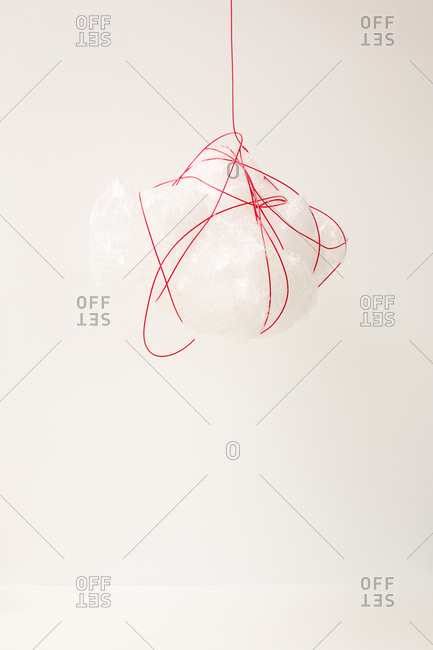 Plastic bag tied and hung with red plastic cord against white wall background