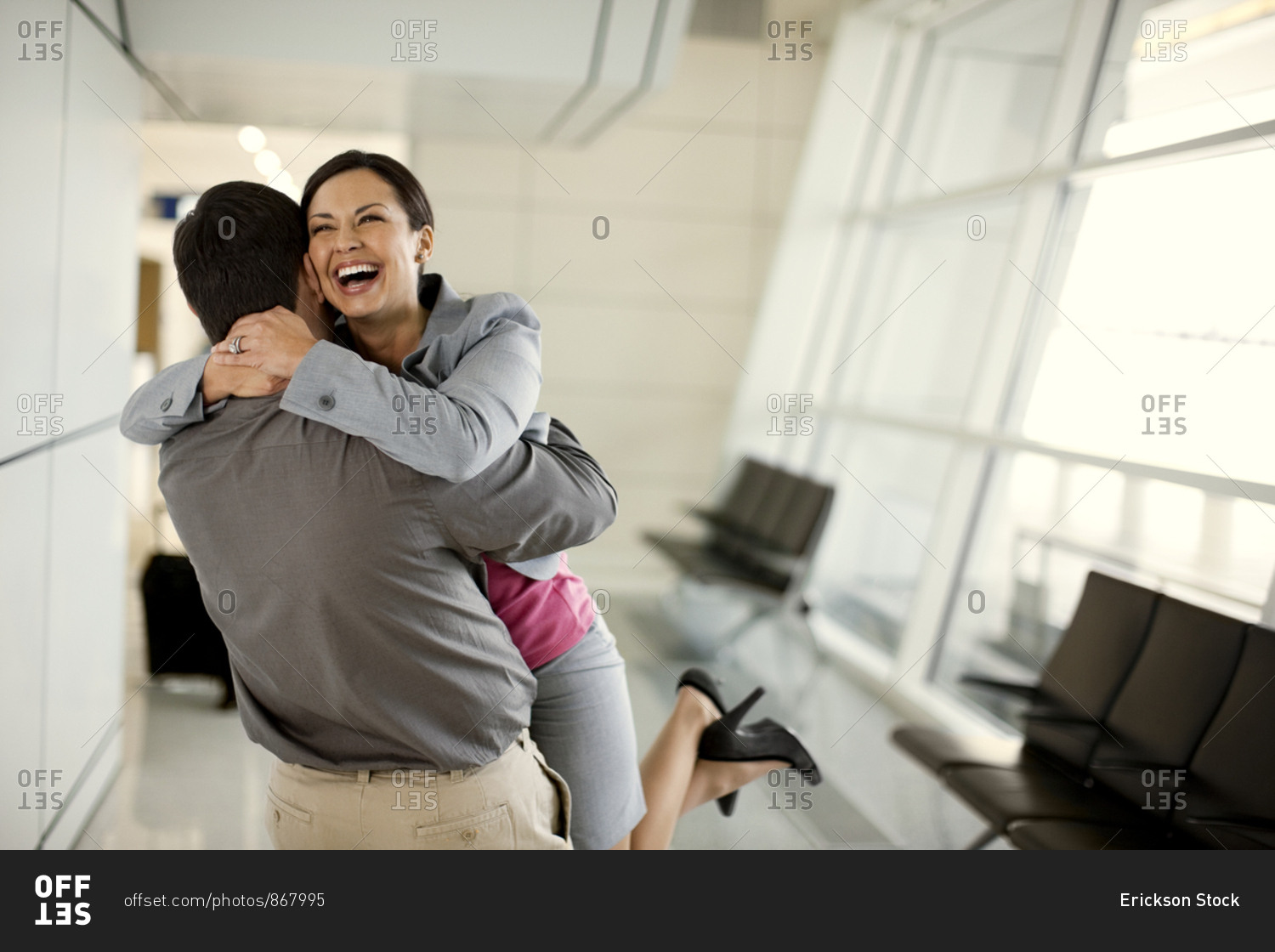 Mid adult woman grins happily as she joyfully hugs her husband who has met her at the airport arrivals gate.