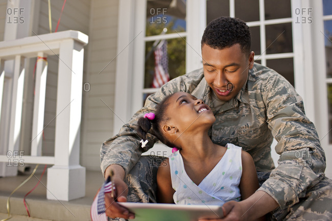 Smiling young girl looking at a digital tablet with her father on the front porch.