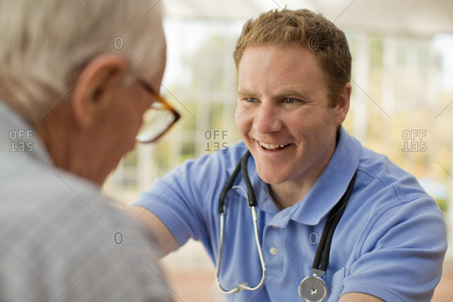 Smiling male nurse encouraging his elderly male patient as he talks with him.