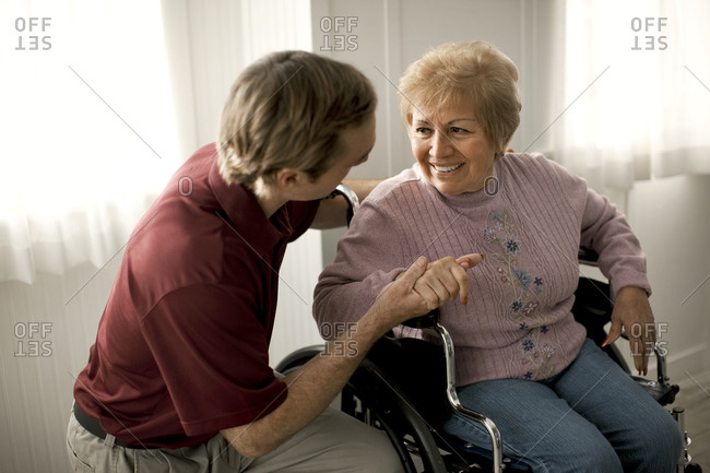 Smiling senior woman talking with a male nurse and being comforted while sitting in a wheelchair.
