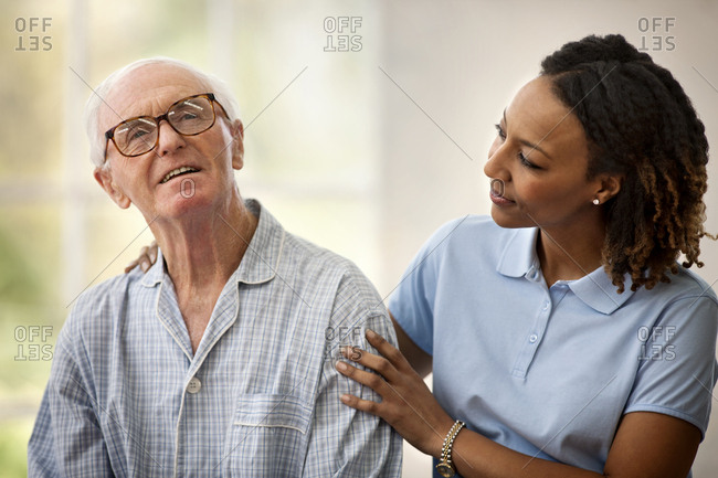 Female nurse listening to an elderly male patient while resting her hand on his shoulder.