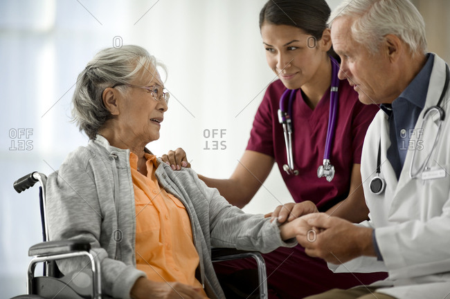 Doctor and nurse speaking to an elderly patient in a wheelchair.