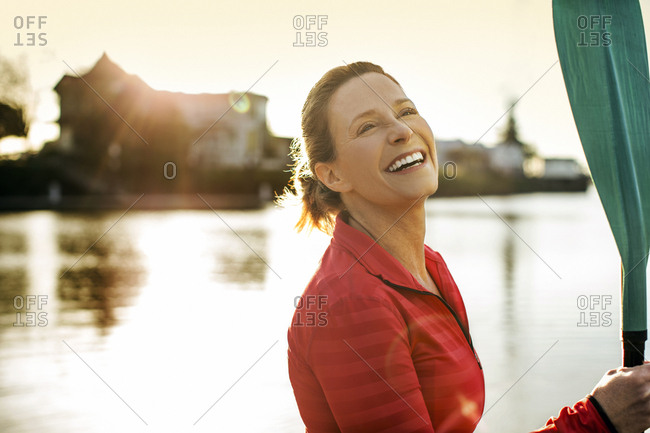 Portrait of a happy paddleboarder holding her oar by a lake.