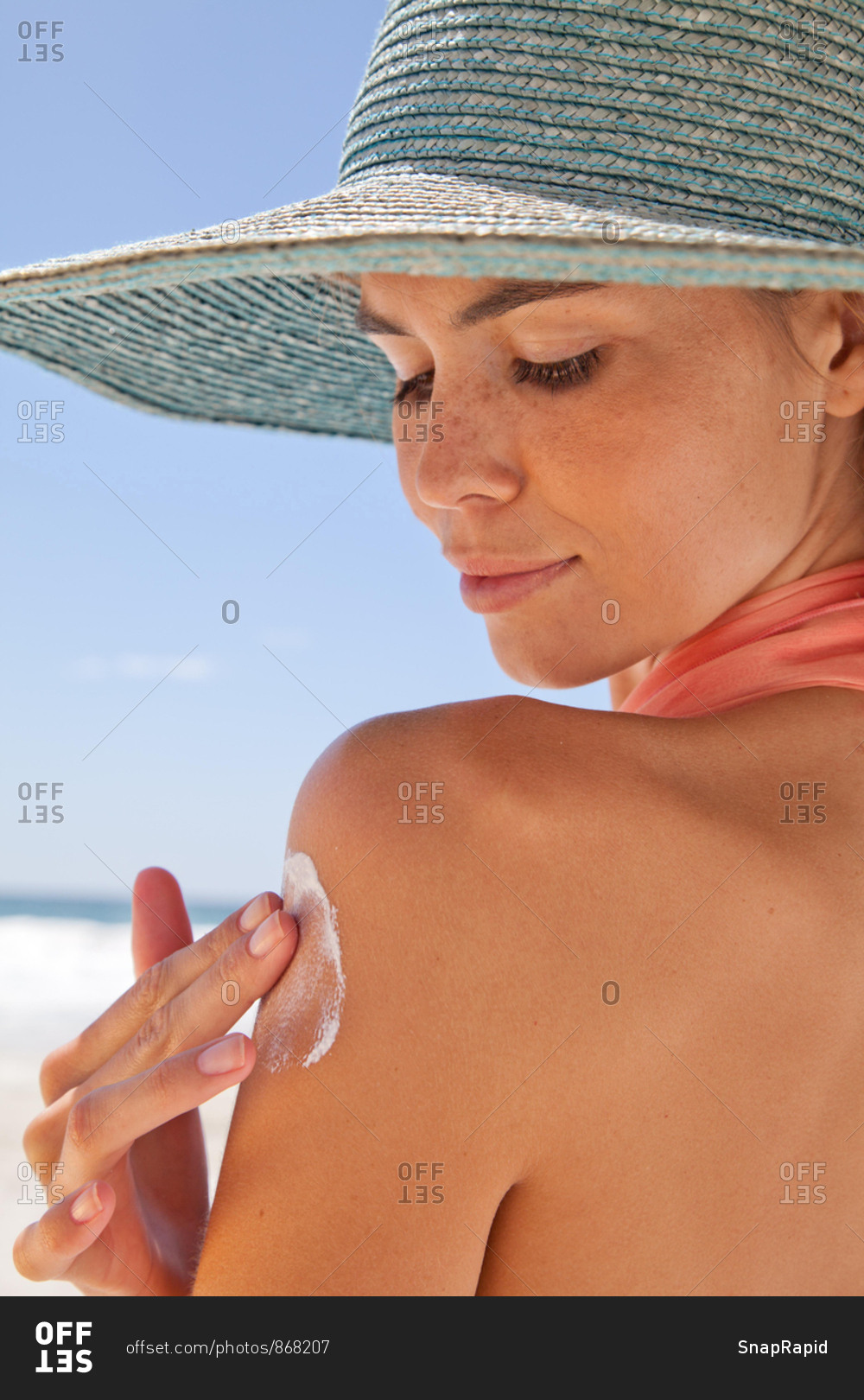Close up of young woman on the beach applying sun cream
