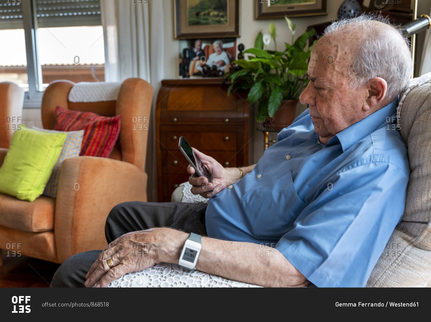 Elderly man using a mobile phone and wearing a smart emergency alarm bracelet around wrist at home
