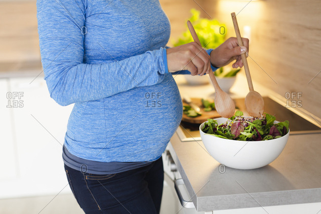 Pregnant woman preparing fresh salad in the kitchen