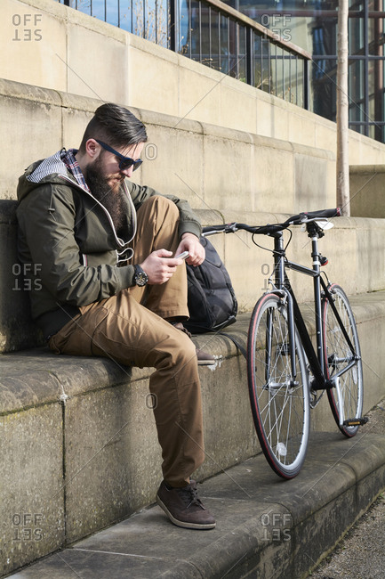 Side view of mid adult man using smart phone while sitting on steps in city