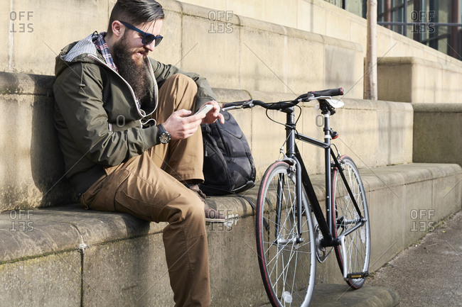 Side view of bearded mid adult man using smart phone while sitting on steps in city