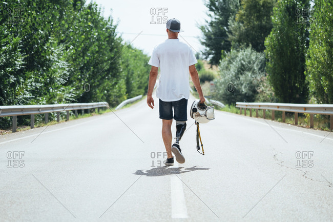 Young man with leg prosthesis walking along the road with a helmet