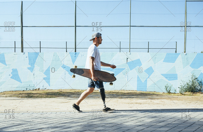 Young man with leg prosthesis walking and holding skateboard