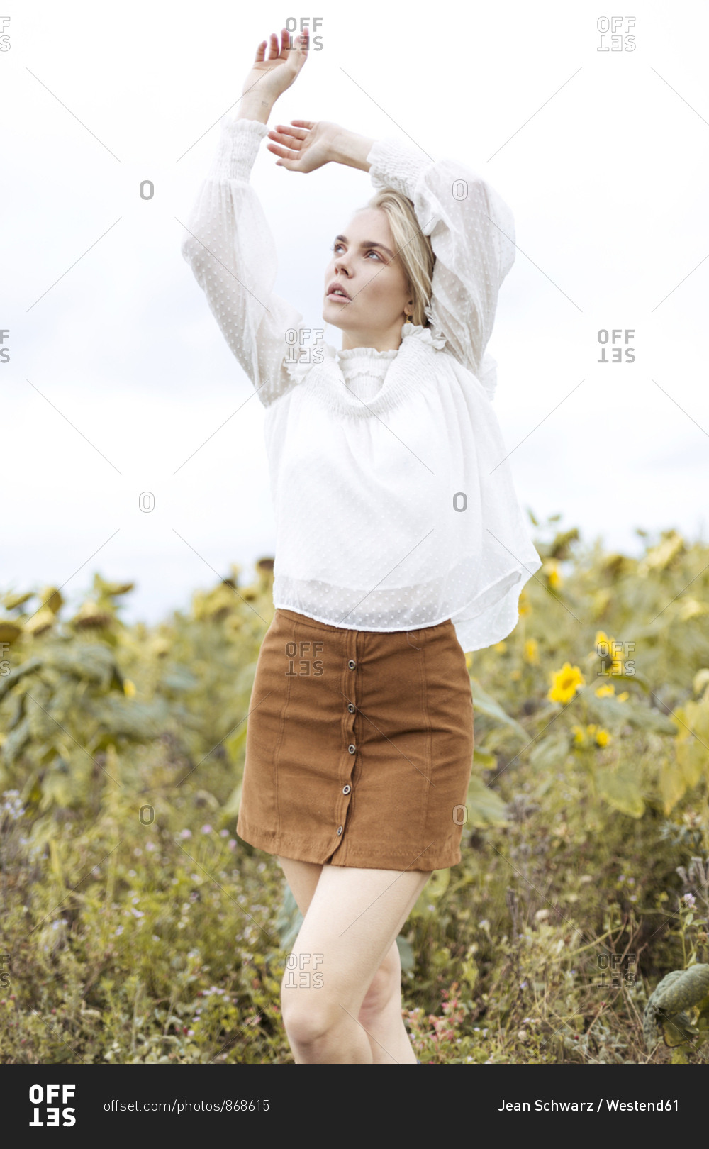 Portrait of blond young woman wearing white blouse dancing on sunflower ...