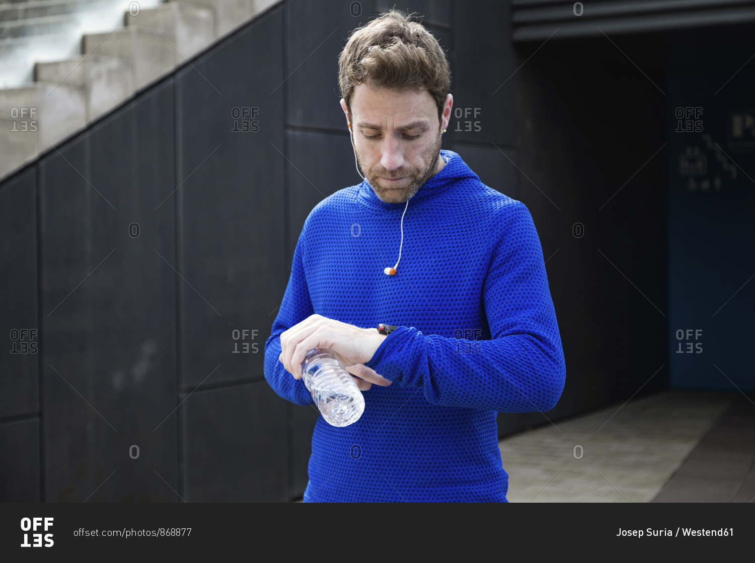 Portrait of jogger with water bottle- checking workout progress on his smart watch