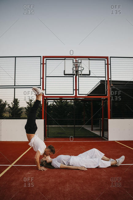 Young couple on a basketball ground- woman lying and man doing a handstand and kissing her