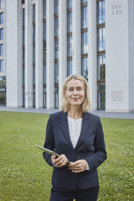 Portrait of confident businesswoman with tablet standing on lawn in the city