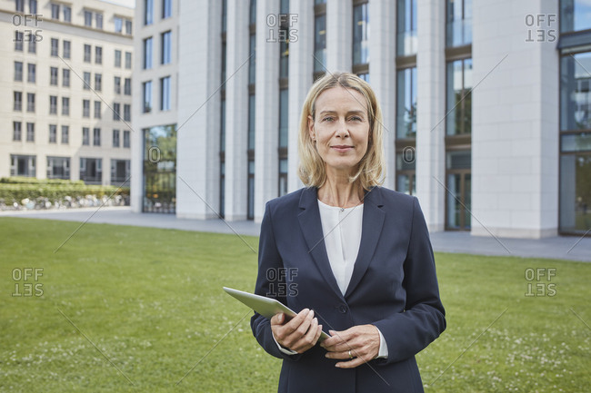 Portrait of confident businesswoman with tablet standing on lawn in the city