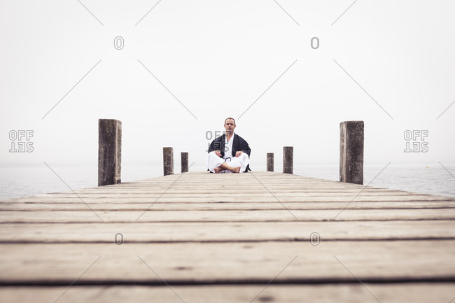 Man sitting on jetty doing yoga exercise- Lake Starnberg- Germany