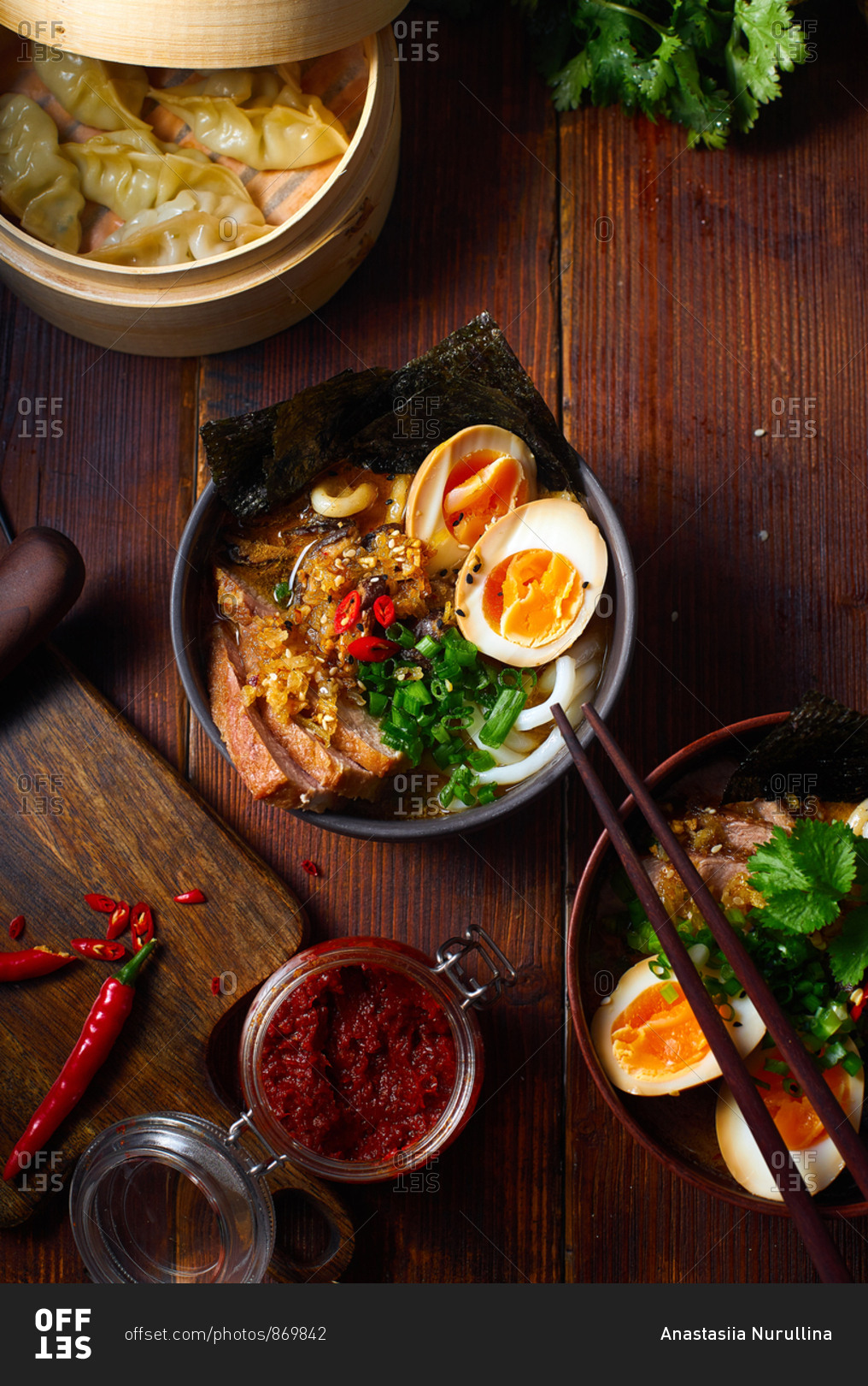 Asian cuisine dishes: pork ramen with soy-marinated eggs and gyoza dumplings served in a bamboo steamer on wooden background