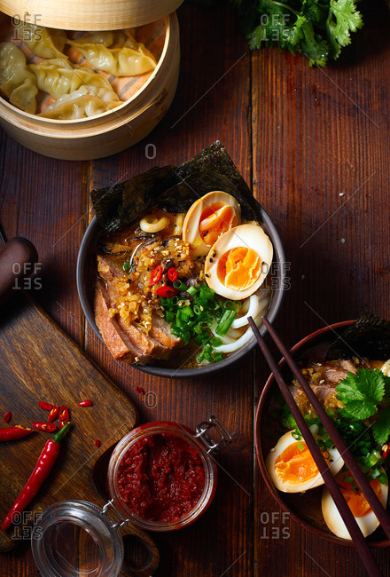 Asian cuisine dishes: pork ramen with soy-marinated eggs and gyoza dumplings served in a bamboo steamer on wooden background