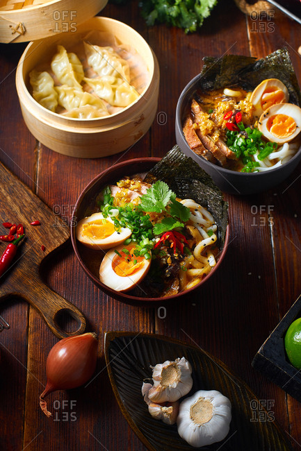 Asian cuisine dishes: pork ramen with soy-marinated eggs and gyoza dumplings served in a bamboo steamer on wooden background