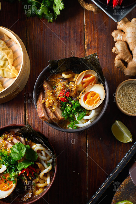 Asian cuisine dishes: pork ramen with soy-marinated eggs and gyoza dumplings served in a bamboo steamer on wooden background