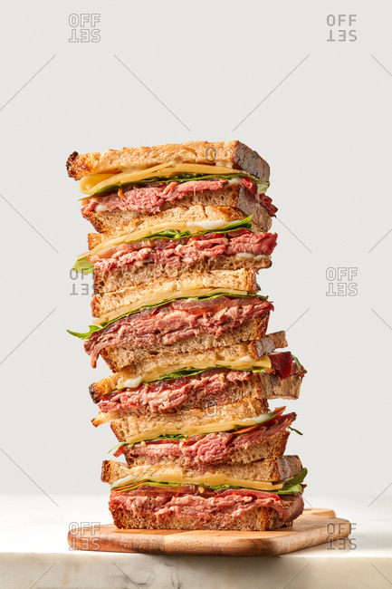 Very big homemade burger with delicious ham, cheese and fresh vegetables lettuce on a wooden board and light grey background, copy space.