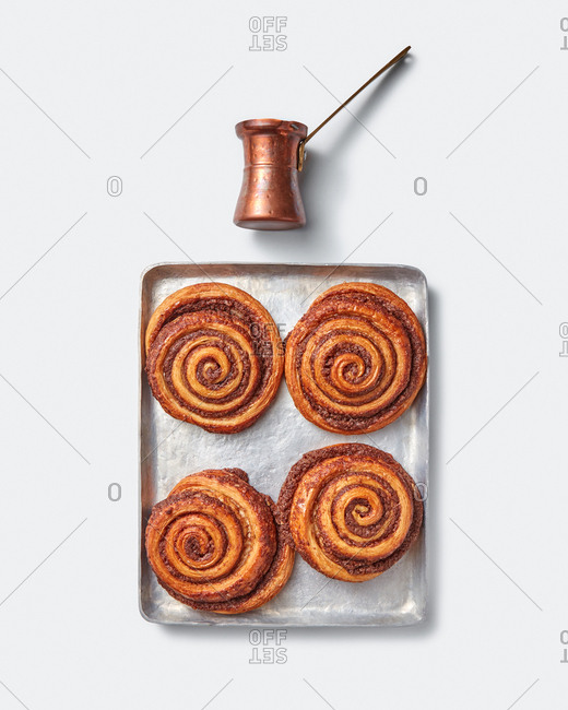 Homemade freshly baked cinnamon buns on a square sheet with coffee maker on a light grey background, copy space. Top view.