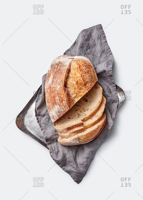 Slices of freshly baked natural organic wholegrain bread on a baking sheet with textile towel on a light grey background, copy space. Top view.